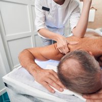 Close up of man lying on massage table while masseuse massaging his back with elbow
